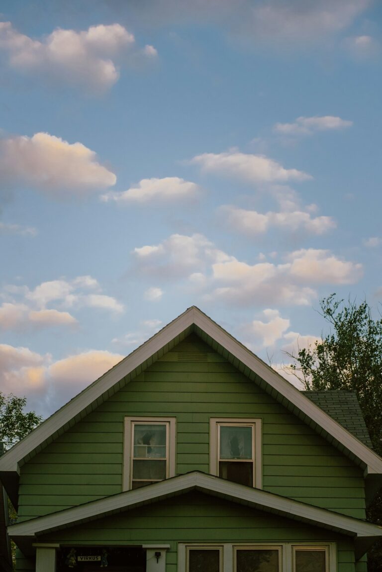 A residential home with clean vinyl siding, white trim, and a worker inspecting panels near a window.